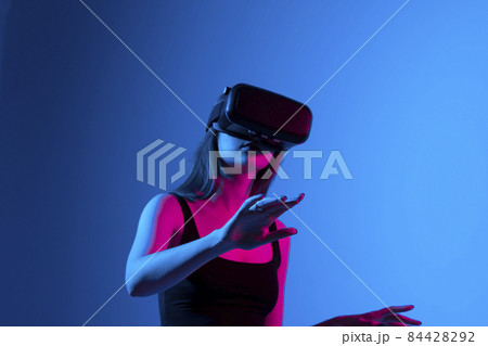 Woman enjoying a VR experience. Woman with VR headset touching invisible screen. Future technology concept. 84428292
