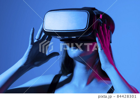 Young woman using VR headset helmet to interacts with metaverse using swipe and stretching gestures. Watching virtual reality 3d video. Girl in VR goggles looking around. Young woman using VR headset helmet to interacts with metaverse using swipe and stretching gestures. Watching virtual reality 3d video. Girl in VR goggles looking around. 84428301