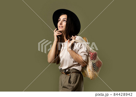 Woman in a beige t-shirt and a hat holding mesh shopping bag with groceries. Conscious consumption. Eco trend. Zero waste concept. Girl carry bag shopper. Woman in a beige t-shirt and a hat holding mesh shopping bag with groceries. Conscious consumption. Eco trend. Zero waste concept. Girl carry bag shopper. 84428942