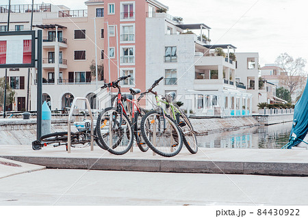 Bicycles are parked on the embankment. Bicycle parking in the background of modern houses. Urban backdrop for branding, banner, cover, card, poster, header for website. High-Quality Horizontal Photo Bicycles are parked on the embankment. Bicycle parking in the background of modern houses. Urban backdrop for branding, banner, cover, card, poster, header for website. High-Quality Horizontal Photo 84430922