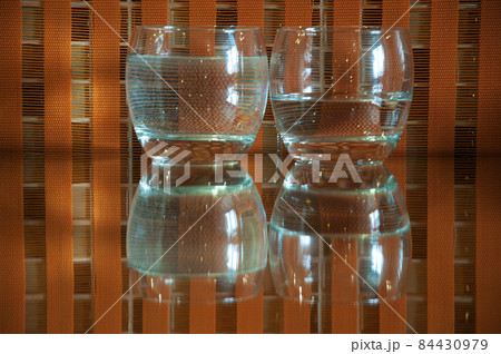 2 glasses with water and reflections on an orange checkered background 2 glasses with water and reflections on an orange checkered background 84430979