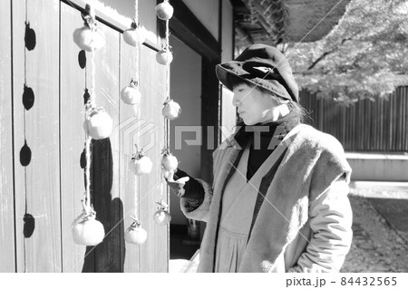 旅先で民家の軒先にある干し柿の横にいる女性 旅先で民家の軒先にある干し柿の横にいる女性 84432565