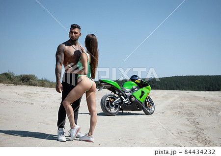 Confident man and young female standing and hugging against motorbike in countryside 84434232
