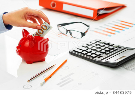 Hand putting hundred dollars note into piggy coins bank 84435979