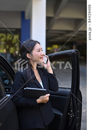 Confident businesswoman standing near her car and talking on mobile phone. Confident businesswoman standing near her car and talking on mobile phone. 84439406