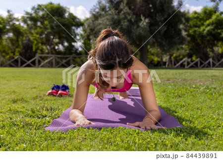 Young concentrated woman in plank position on mat in a park in a summer day 84439891