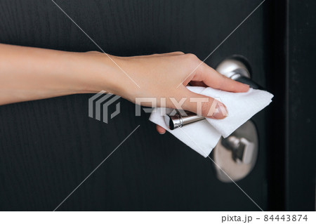 Cleaning black door handles with an antiseptic wet wipe. Sanitize surfaces prevention in hospital and public spaces against corona virus. Woman hand using towel for cleaning home room door link. 84443874