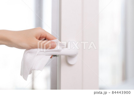 Cleaning door handles with an antiseptic wet wipe and gloves. Sanitize surfaces prevention in hospital and public spaces against corona virus. Woman hand using towel for cleaning home room door link. 84443900