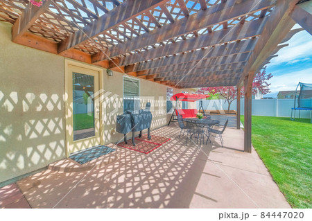 Backyard patio with attached wooden pergola roof and covered barbecue griller Backyard patio with attached wooden pergola roof and covered barbecue griller 84447020