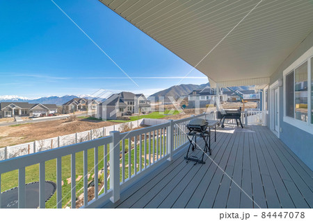 Backyard deck of a house with barbecue grills and a lawn with tarpauline and vinyl fence 84447078