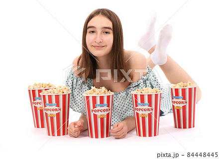 Girl lies on the floor with buckets of popcorn.. Isolated on white. 84448445