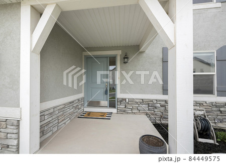 Front porch with light gray door with side window glass panel, doormat and stone bricks wall 84449575