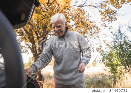 Man standing near the open trunk of his car and smiling while preparing for the walking Man standing near the open trunk of his car and smiling while preparing for the walking 84449731