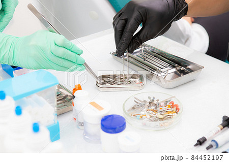 Dental burs in a glass bowl while the dentist takes one. Two dentists are choosing an instrument Dental burs in a glass bowl while the dentist takes one. Two dentists are choosing an instrument 84452197