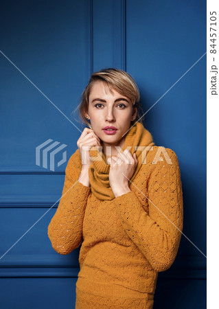 Studio portrait of a young woman in yellow pullover on blue wall background. 84457105
