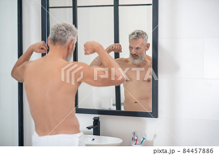 Man straining muscles of arms looking in mirror 84457886