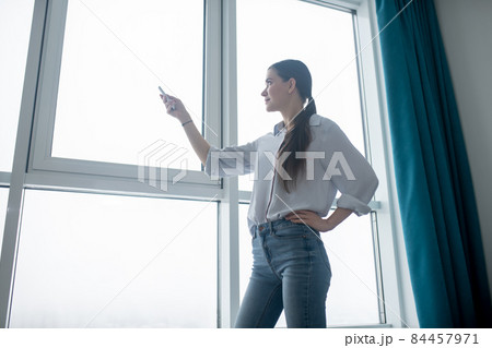 Concentrated lady using a remote control for closing the blinds Concentrated lady using a remote control for closing the blinds 84457971