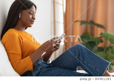 African American Female Using Cellphone Wearing Wireless Earbuds At Home African American Female Using Cellphone Wearing Wireless Earbuds At Home 84461183