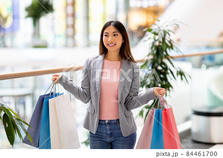 Portrait of beautiful young Asian woman holding colorful gift bags in both hands, shopping at city mall Portrait of beautiful young Asian woman holding colorful gift bags in both hands, shopping at city mall 84461700