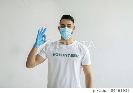 Voluntary free work, charity grace concept. Male volunteer in medical mask and gloves showing OK gesture, light wall Voluntary free work, charity grace concept. Male volunteer in medical mask and gloves showing OK gesture, light wall 84461932