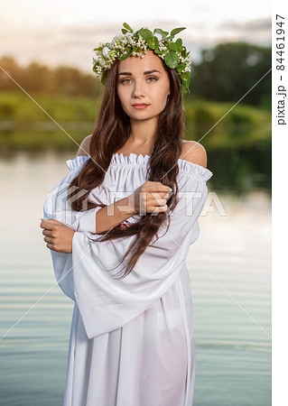 Beautiful black haired girl in white vintage dress and wreath of flowers standing in water of lake. Sun flare. Beautiful black haired girl in white vintage dress and wreath of flowers standing in water of lake. Sun flare. 84461947