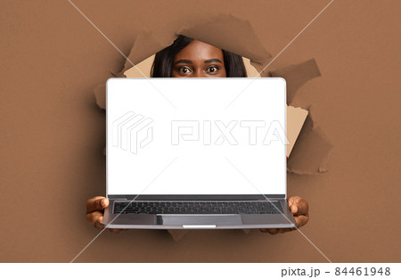 Black young lady showing empty laptop screen through torn paper Black young lady showing empty laptop screen through torn paper 84461948