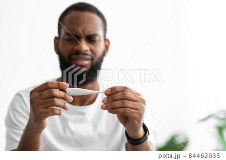 Sad young african american guy with beard looks at thermometer and feeling bad on white background Sad young african american guy with beard looks at thermometer and feeling bad on white background 84462035