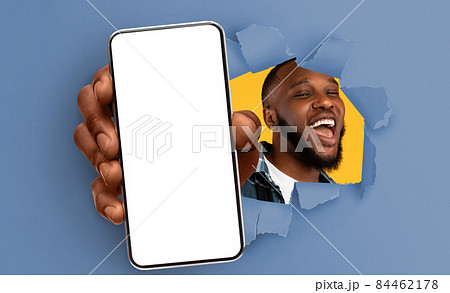 Black guy showing white empty smartphone screen through torn paper 84462178
