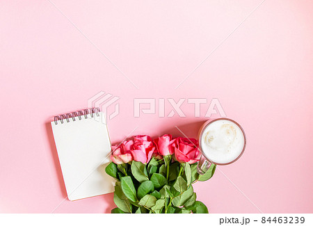 The cup of hot coffee, empty notepad with funny pen and bouquet of fresh roses on soft pink background. The cup of hot coffee, empty notepad with funny pen and bouquet of fresh roses on soft pink background. 84463239