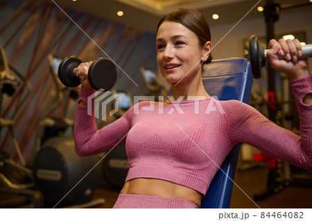 Middle aged muscular beautiful athletic woman doing exercise for arms, working out with dumbbells at gym. Strength and motivation concept. Healthy lifestyle, sport, fitness 84464082