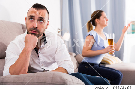 Sad male is sitting alone when his wife is watching TV Sad male is sitting alone when his wife is watching TV 84473534
