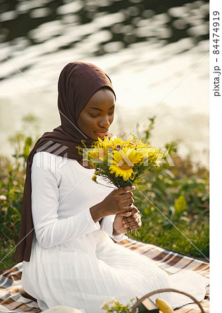 Portrait of a muslim woman sits on the plaid picnic blanket near the river Portrait of a muslim woman sits on the plaid picnic blanket near the river 84474919