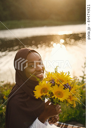 Portrait of a muslim woman sits on the plaid picnic blanket near the river Portrait of a muslim woman sits on the plaid picnic blanket near the river 84474921