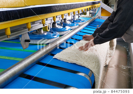 Laundry worker in the process of working on automatic machine for carpet washing in dry cleaning Laundry worker in the process of working on automatic machine for carpet washing in dry cleaning 84475093