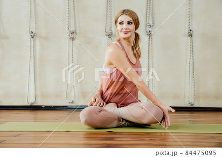 Mature woman practicing yoga sitting in twisting pose on a floor Mature woman practicing yoga sitting in twisting pose on a floor 84475095