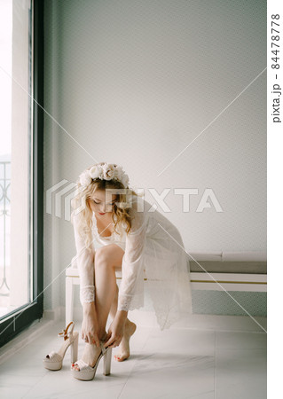 Bride in white lace peignoir wears high-heeled sandals in preparation for the wedding ceremony Bride in white lace peignoir wears high-heeled sandals in preparation for the wedding ceremony 84478778