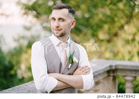 Groom crossed his arms over his chest near the balustrade in the garden. Portrait 84478942