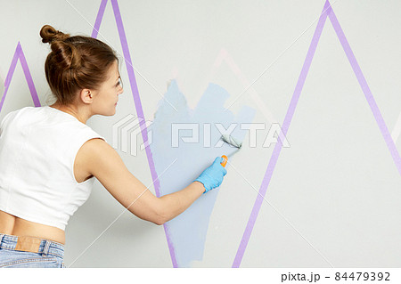 Back view of girl painting wall with paint roller and using masking tape while standing on ladder Back view of girl painting wall with paint roller and using masking tape while standing on ladder 84479392