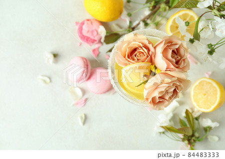 Glass of cocktail, ingredients and flowers on white textured table 84483333