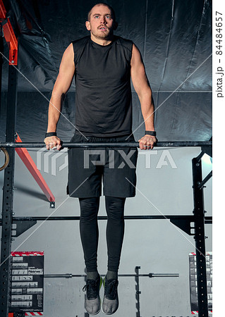 Young man flexing abdominal muscles on pull-up bar in gym 84484657