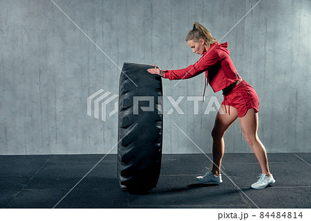 Fit female athlete working out with a huge tire, turning and flipping in the gym. 84484814