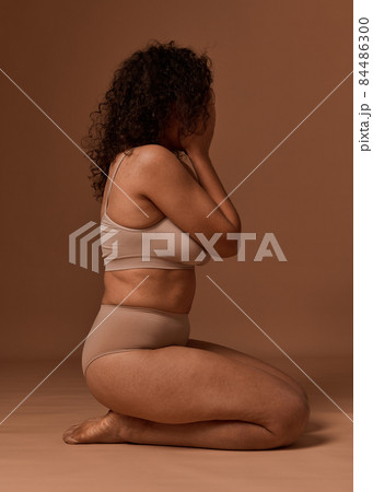 Depressed woman in lingerie with cellulite and stretch marks closes her eyes, sitting against a beige background, does not accept herself and her body because of the framework established by society. Depressed woman in lingerie with cellulite and stretch marks closes her eyes, sitting against a beige background, does not accept herself and her body because of the framework established by society. 84486300