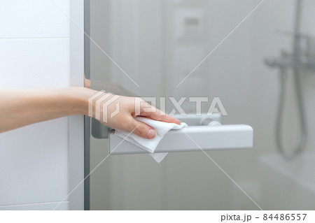 Cleaning glass door handles with an antiseptic wet wipe. Sanitize surfaces prevention in hospital and public spaces against corona virus. Woman hand using towel for cleaning home room door link. 84486557