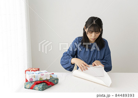 リビングのテーブルで贈り物を包装紙で包む女性 84489393