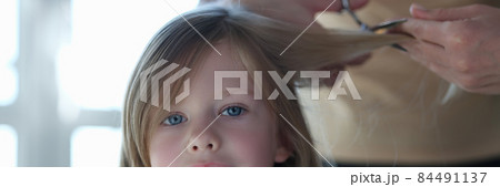 Woman scissors hair of cute blonde little girl closeup 84491137