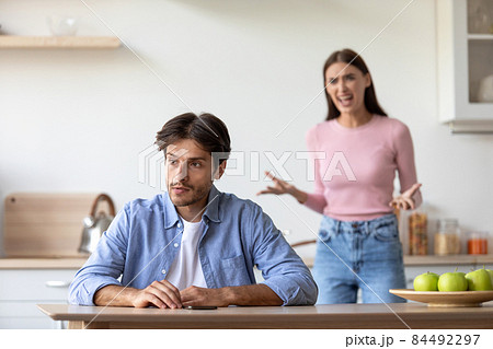Angry aggressive millennial european wife yells at sad depressed husband at kitchen Angry aggressive millennial european wife yells at sad depressed husband at kitchen 84492297