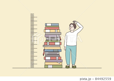 Boy measuring growth stand near books pile 84492559