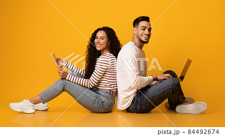 Cheerful arab couple sitting back to back with laptop and digital tablet 84492674