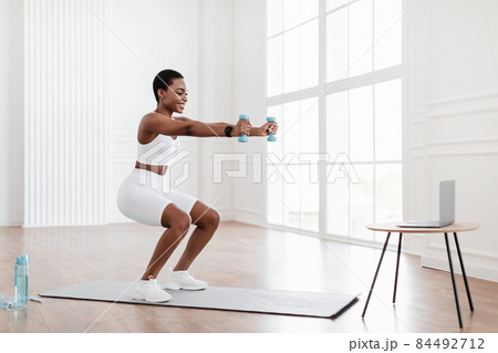 Young black woman exercising with dumbbells in front of laptop Young black woman exercising with dumbbells in front of laptop 84492712
