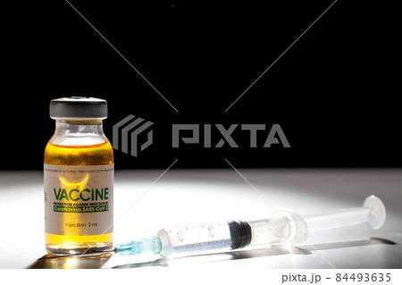 A vial with a medicine for coronavirus on a white table and a syringe. Black background and beam of light, copy space for text, macro A vial with a medicine for coronavirus on a white table and a syringe. Black background and beam of light, copy space for text, macro 84493635